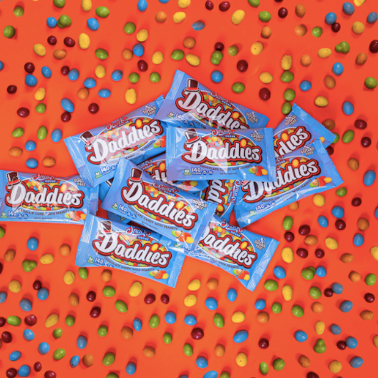 Daddies chocolate peanut candies in their baby blue package on an orange background with various candies scattered around